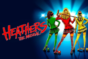 Poster for Heathers: The Musical showing three girls in colorful outfits seen from behind, holding croquet mallets against a blue spotlight background, with the red Heathers logo on the left.