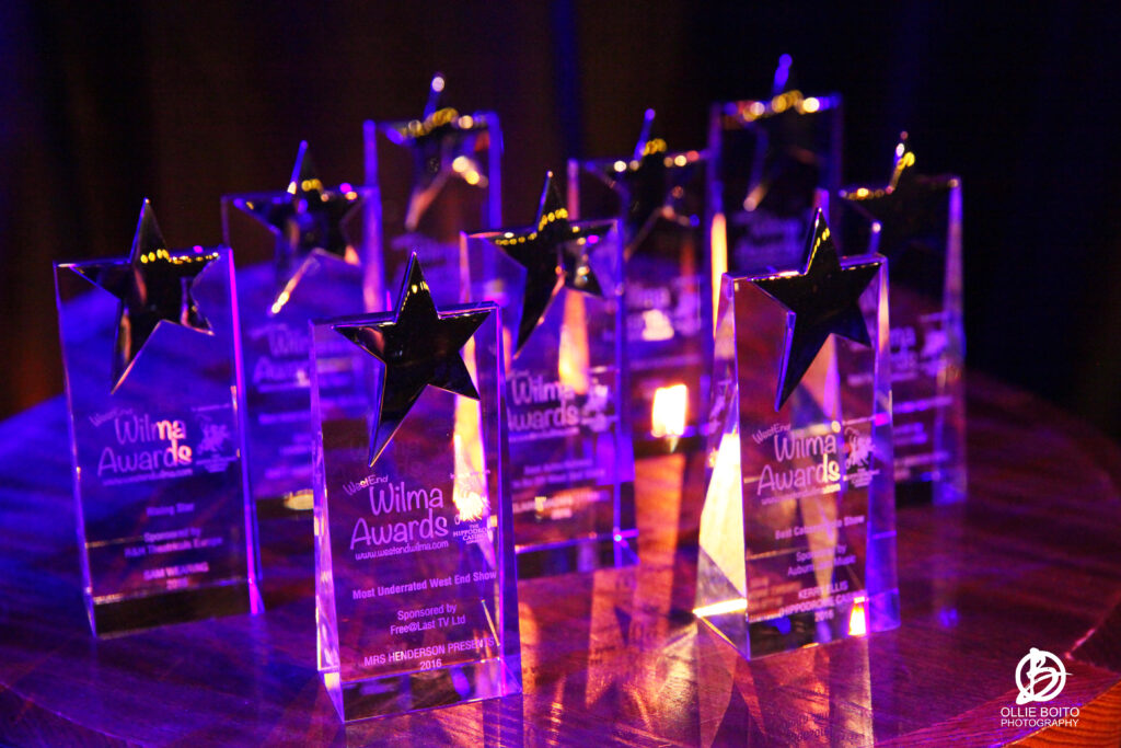Row of crystal star trophies lit in purple lighting, each engraved with 'Wilma Awards'.