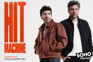 Promotional poster for Hit Machine at Soho Theatre, featuring two men against a white background with bold orange 'HIT MACHINE' text and the tagline 'One Song Could Save You.'