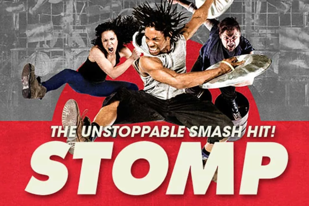 Promotional poster for STOMP showing three dancers mid-jump against a red backdrop with bold white title text.